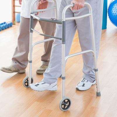 A man walking with a zimmer frame indoors on a light wood floor.