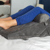 a woman using the bed wedge pillow to elevate her legs in bed