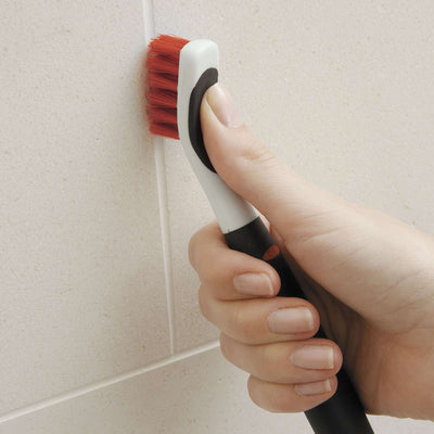 a hand gripping an oxo deep clean brush and using it to clean grout between tiles