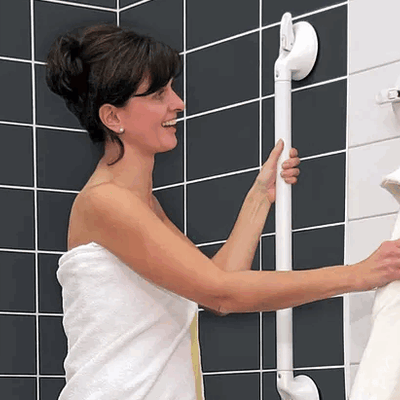 shows a woman wrapped in a towel, using a Mobeli Grab Handle in a shower cubicle