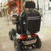 shows the Flexi Mobility Bag Large attached to the back of a mobility scooter with a walking stick/cane in either of the crutch/stick holders