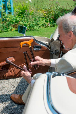 the image shows a man using a classic canes folding derby cane to help him to safely get of a car.