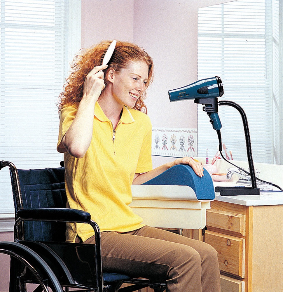 shows a young woman in a wheelchair, using the Hands Free Hair Dryer Stand to style her hair with one hand