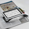 the image shows the eschenbach smartlux 12.7 cm digital magnifier being used to help someone to read a newspaper