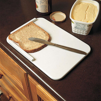shows the homecraft plastic spreading board on a kitchen counter top with a piece of bread and butter knife. A pot of jam and tub of butter spread sit beside the board.