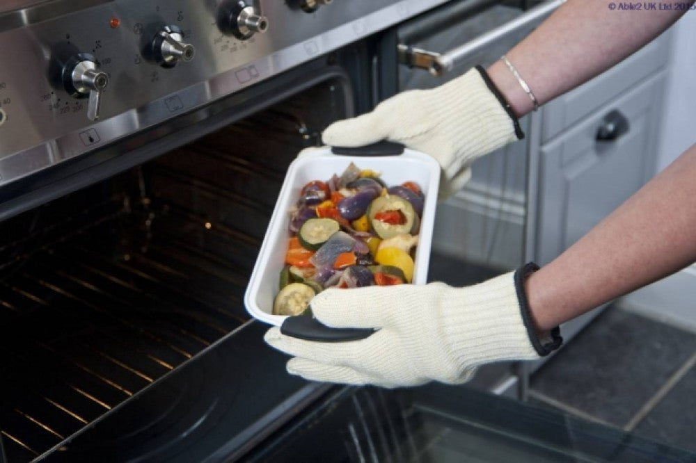 shows someone wearing the anti burn gloves to remove an oven dish of roasted vegetables from an oven