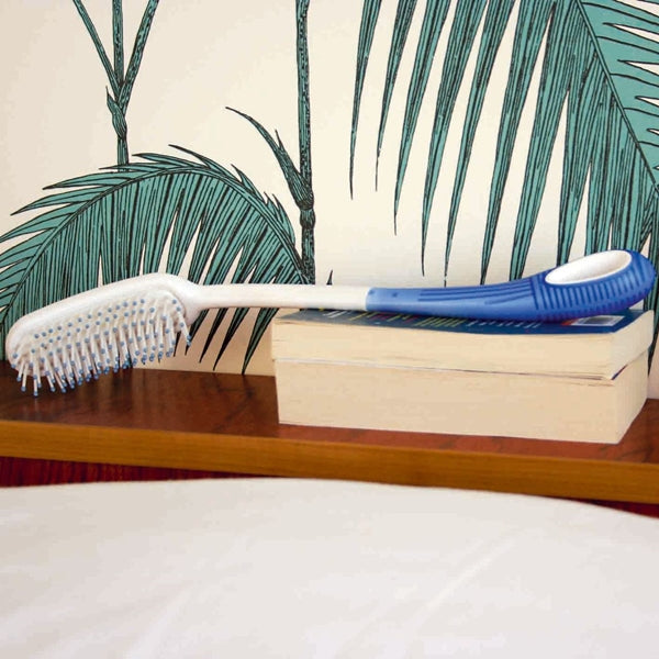 shows an Etac Long Handled Hair Brush resting on some books on a shelf
