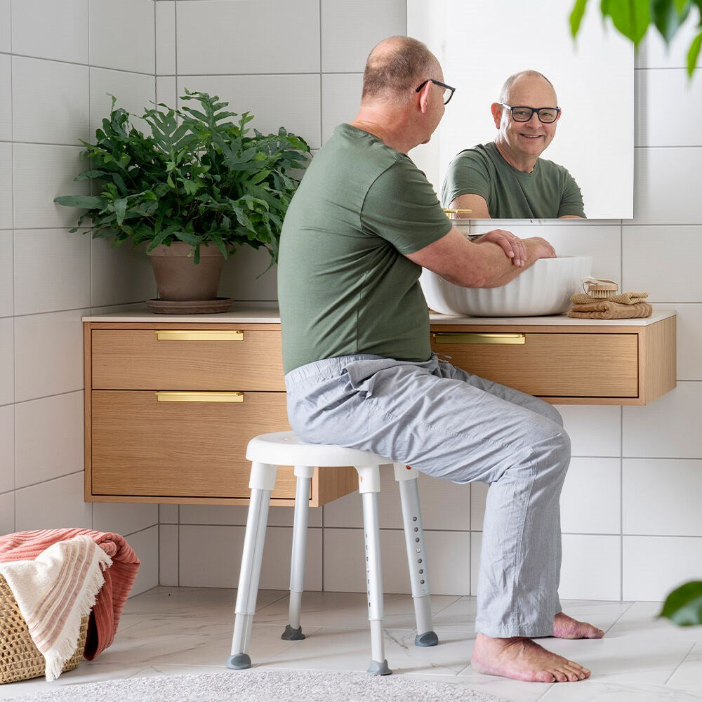 Easy shower stool being sat on by a gentleman washing his hands smiling in the mirror
