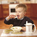 The image shows a happy child eating with an Etac Feed Adjustable Spoon
