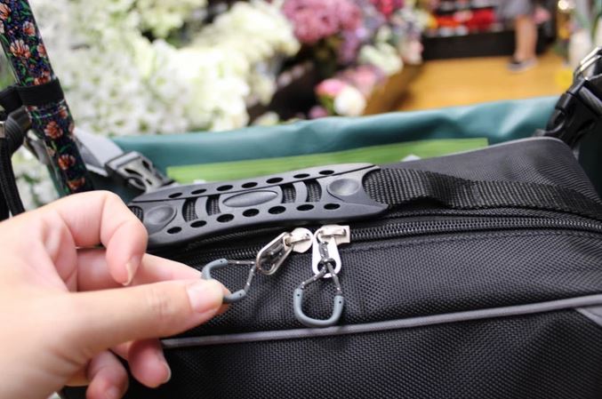 The image shows a close-up of a woman's hand gripping the easy-pull zips on the Hi-Vis Flexi Mobility Bag