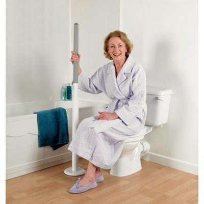 image shows a woman in a dressing gown and slippers sitting on a closed toilet lid, holding on to the Floor Mounted Advantage Grab Rail