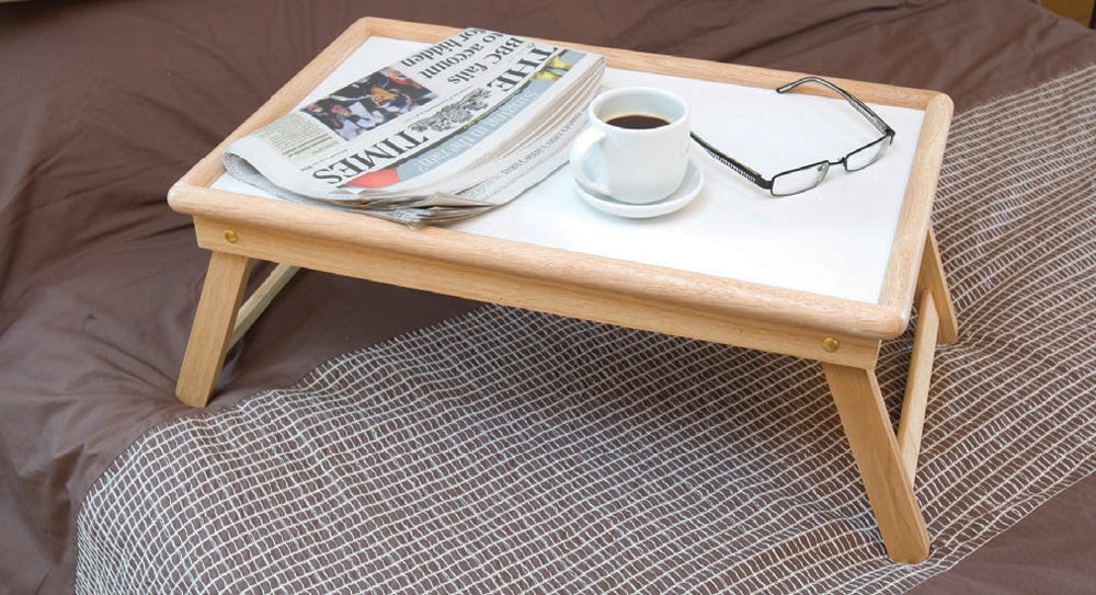 shows the adjustable tray with a paper, coffee, and glasses on it, resting on a bed.