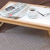 shows the adjustable tray with a paper, coffee, and glasses on it, resting on a bed.