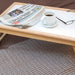 shows the adjustable tray with a paper, coffee, and glasses on it, resting on a bed.