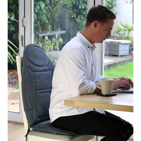 The image shows a man seated at a desk, typing, with the Lifemax heated back and seat massager on his desk chair