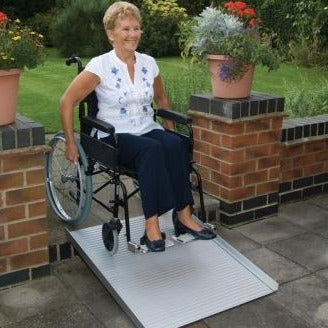 the image shows a woman in a wheelchair using the roll up portable ramp to get down from a step in the garden