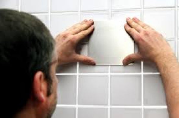 shows a man fixing a Mobeli Cardan Steel Plate to a grey tiled wall