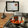the image shows the lifemax hands free mobile device mount being used to hold a tablet in place on a kitchen surface to follow a recipe