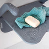 Close up of grey Shower seat with soap and a wash cloth on top of it surrounded by droplets of water