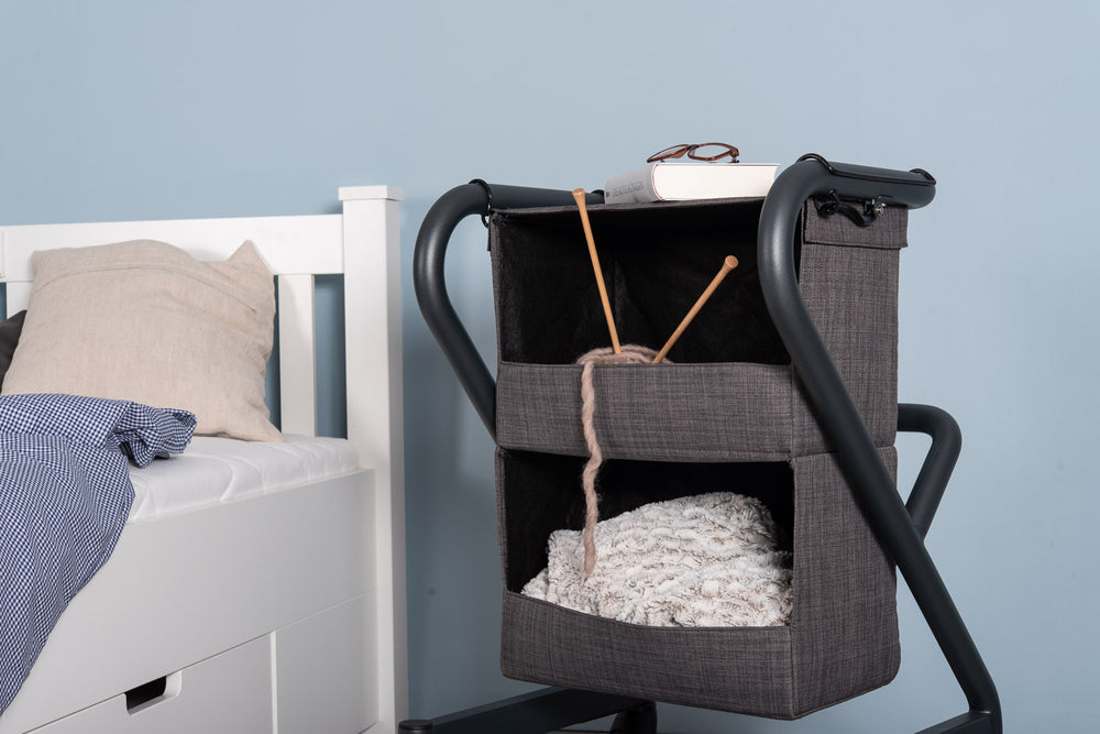 The image shows the bedside cabinet with personal items in the compartments, including knitting and with a book and glasses on the top of the rollator cabinet