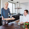 The image shows a young woman using the SALJOL Beech Tray for Page Indoor Rollator to serve food and drink to a young man seated at a table