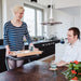 The image shows a young woman using the SALJOL Beech Tray for Page Indoor Rollator to serve food and drink to a young man seated at a table
